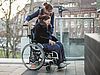 Frau im Rollstuhl wird durch Assistentin begleitet