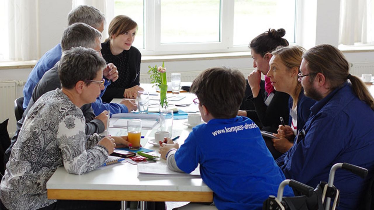 Viele Menschen sitzen an einem Tisch. Sie unterhalten sich.
