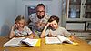 Vater mit zwei Kindenr am Tisch vor Schulbüchern und Heften
