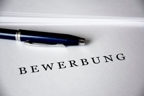 Bewerbung Ein schwarzer Kugelschreiber liegt horizontal auf einem Blatt Papier, auf dem das Wort Bewerbung steht.